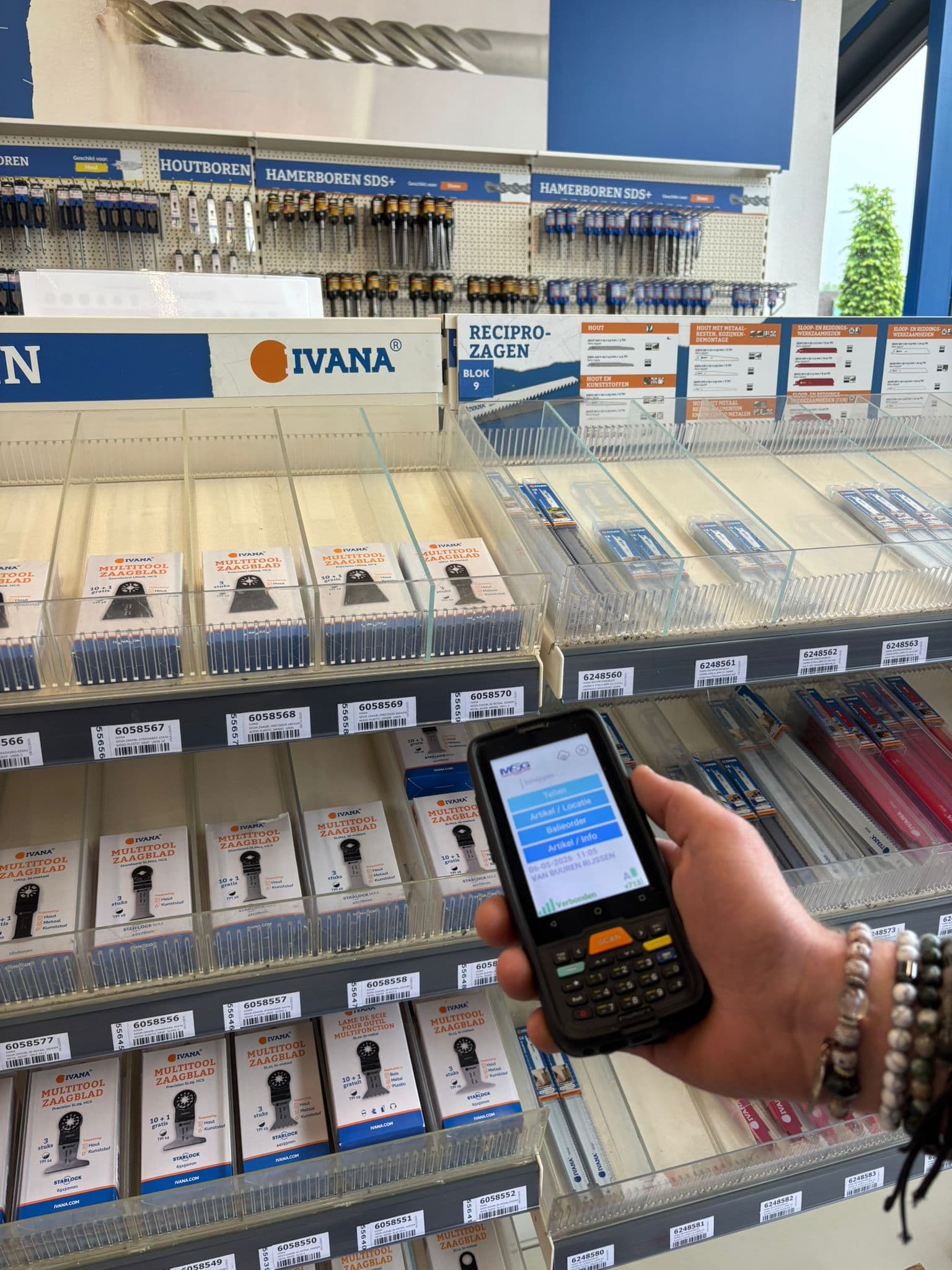 Hand met een scanner met het menu van de MSG scan-app voor de winkelschappen