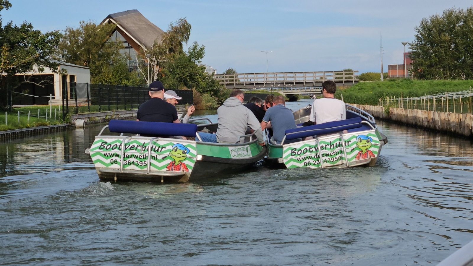 Twee groene huurbootjes van De Zweth varen naast elkaar door een smalle vaart richting een houten brug